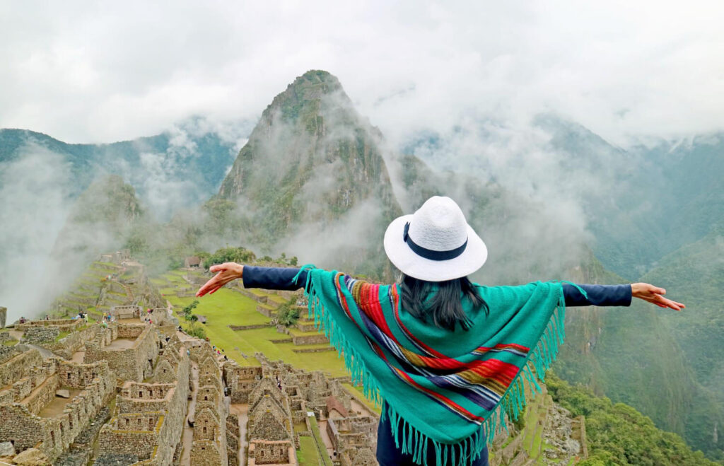 Frau mit Poncho steht auf einem Berg in Peru den Sie in dem besten Peru Reiseführer gefunden hat