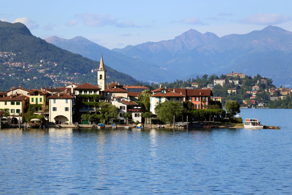 Sonnige Aufnahme von einem Ort mit Kirche am Lago Maggiore mit Bergern im Hintergrund