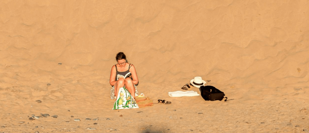 Touristin blättert am Strand in ihrem empfohlenen Gran Canaria Reiseführer im Sand